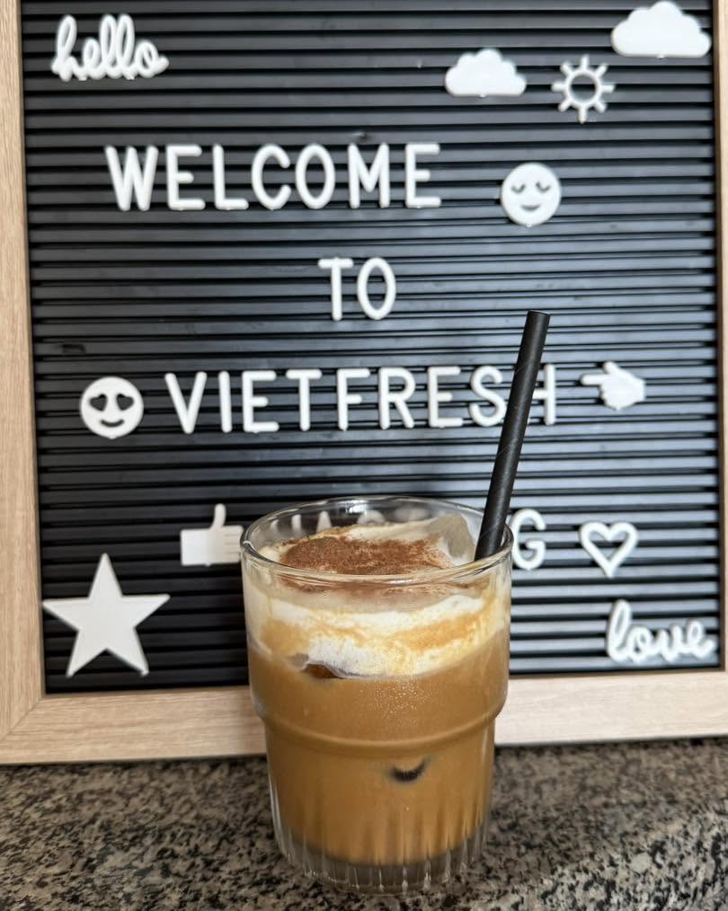 A glass of coffee in front of a letterboard reading Welcome to VietFresh.